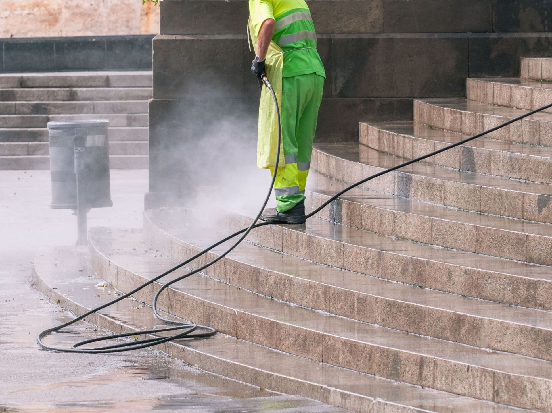 A street worker pressure washes stone stairs in a public park, ensuring cleanliness and safety.